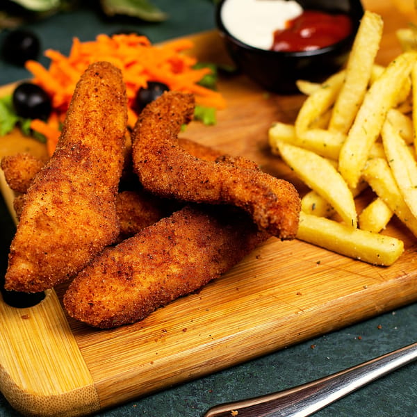 Crispy Rude Rooster chicken tenders, golden fries, and shredded carrots with dipping sauces on a wooden board.