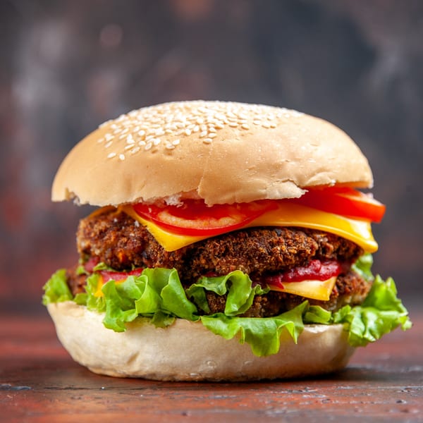 A double-patty burger with cheese, lettuce, tomato, and ketchup on a sesame seed bun.